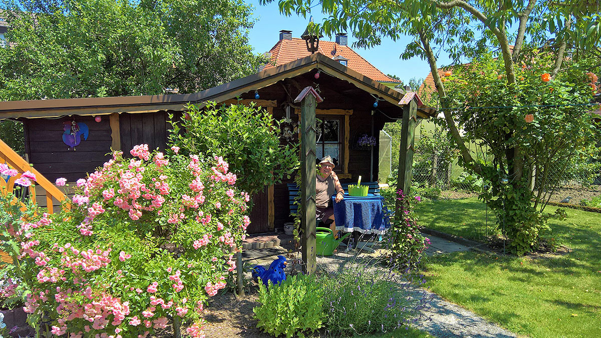 Gartenhaus mit Sitzplatz, üppig blühenden Rosen und Lavendel an einem sonnigen Sommertag – Foto von Heike, Platz 2 beim Gärtner Harry Fotowettbewerb „Dein schönster Garten-Moment im Sommer“